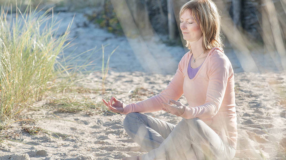 Frau entsptannt beim Yoga am Strand